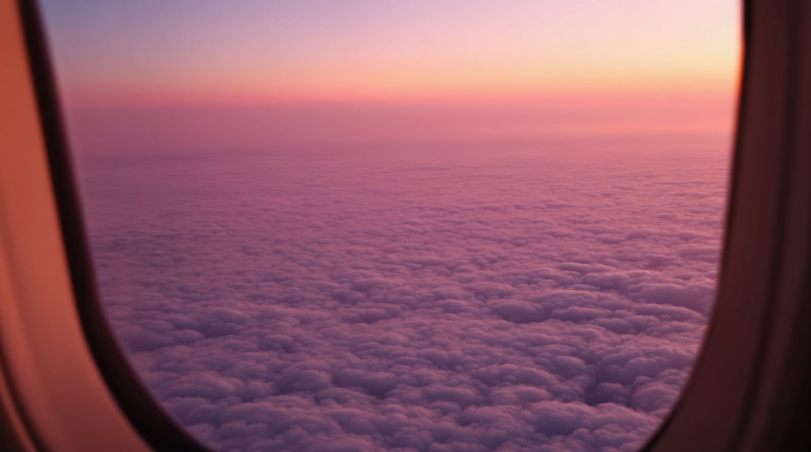 View from an airplane window at sunrise over a sea of pink and gold clouds