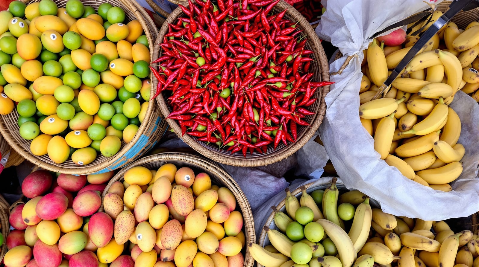 Woven baskets heaped with mangoes, limes, red chilies and bananas at a market stall