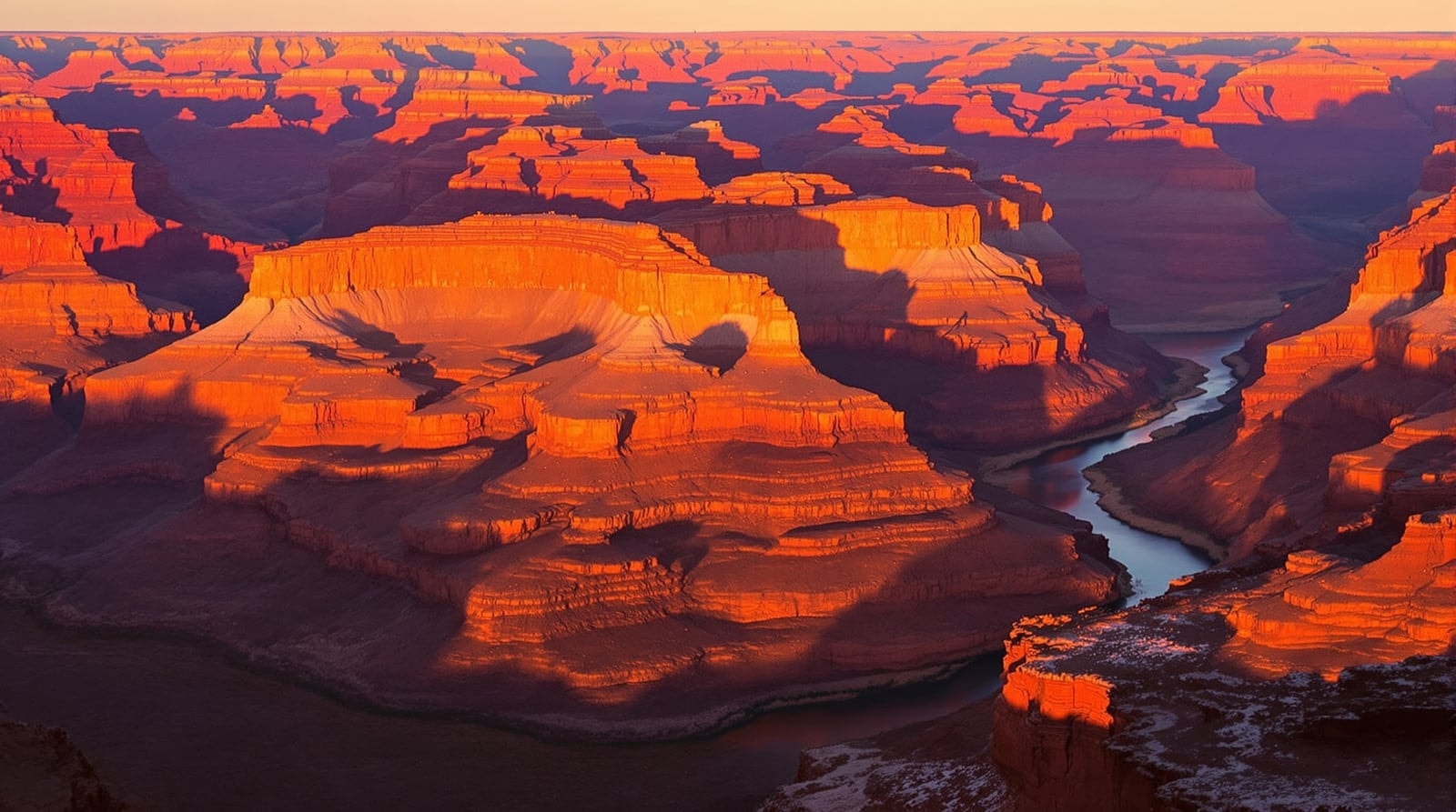 Layered red and orange canyon walls at golden hour with a river winding far below